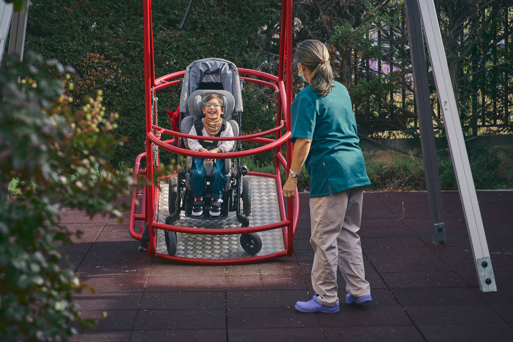 Niño con parálisis cerebral riendose por las sensaciones vestibulares producidas en su cuerpo por el columpio adaptado para su silla.