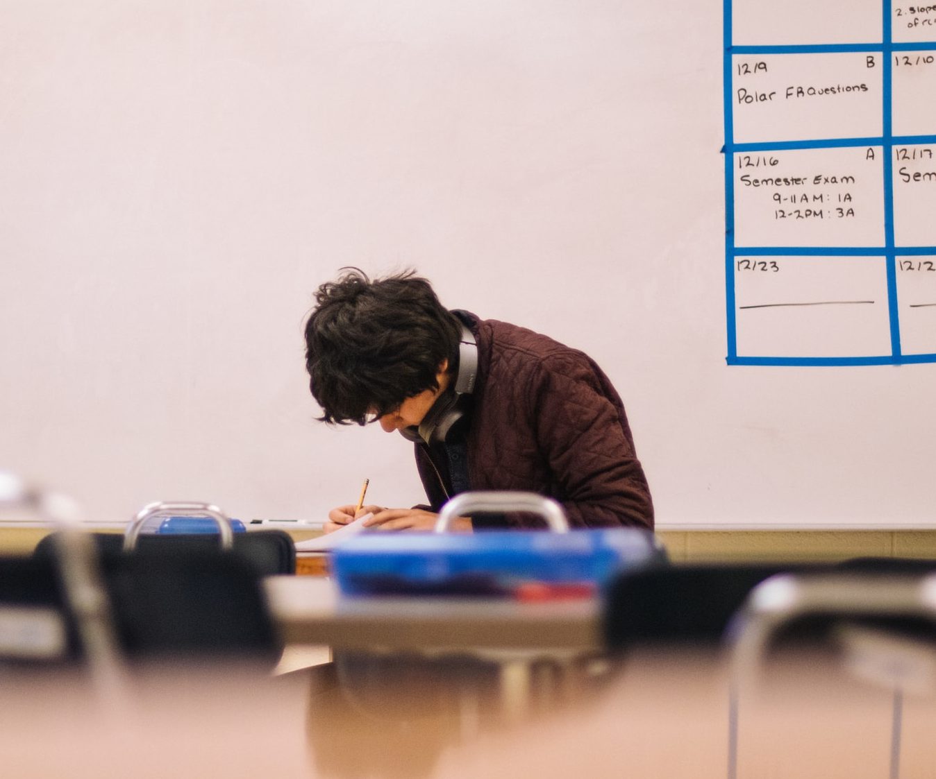 un alumno escribiendo sobre mesa de escritorio en aula