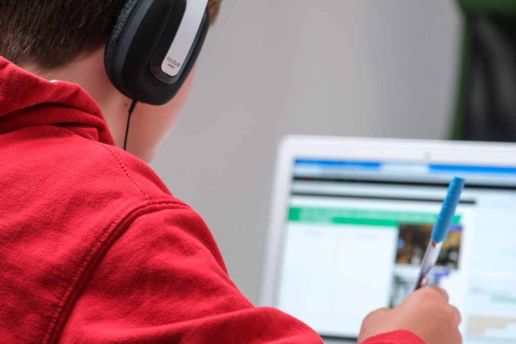 alumno con auriculares puestos escribiendo y mirando una pantalla de ordenador