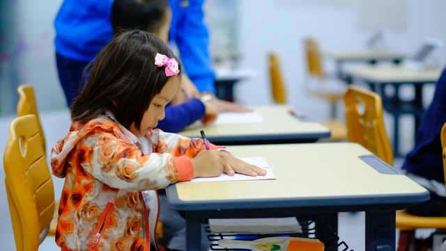 niña escribiendo sobre un escritorio en el aula del colegio
