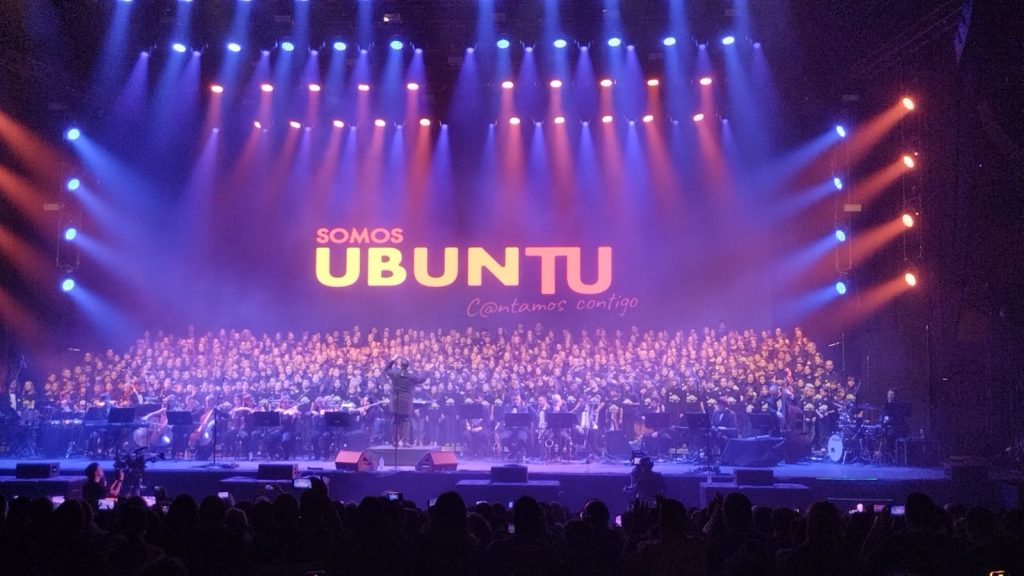 Gran coro escolar y orquesta en el escenario bajo el rótulo «Somos UBUNTU. Cantamos contigo»