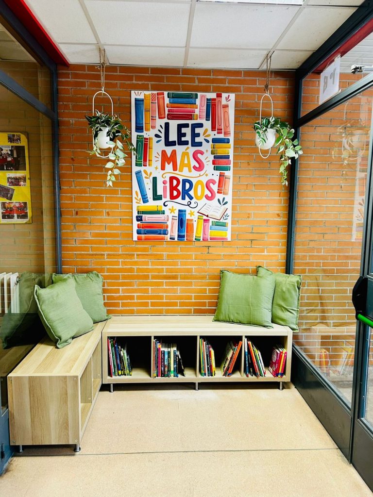 Rincón del Bibliopatio: banco con cojines verdes y estantería llena de libros infantiles y juveniles, bajo el cartel «Lee más libros»