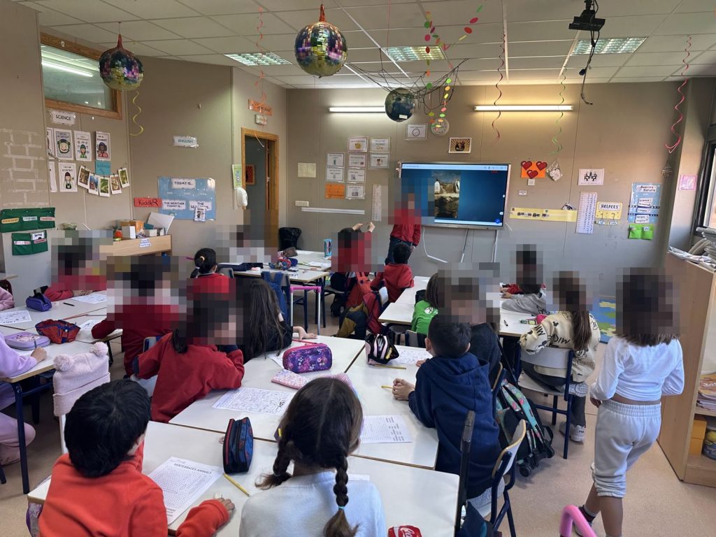 Una alumna expone delante de la clase junto a la pantalla