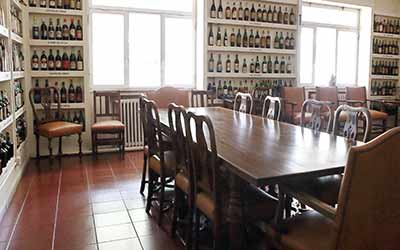 Gran mesa en espacio iluminado y rodeado de estanterías con botellas de vino